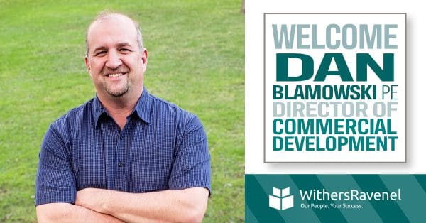 A smiling Dan Blamowski next to a banner welcoming him to WithersRavenel