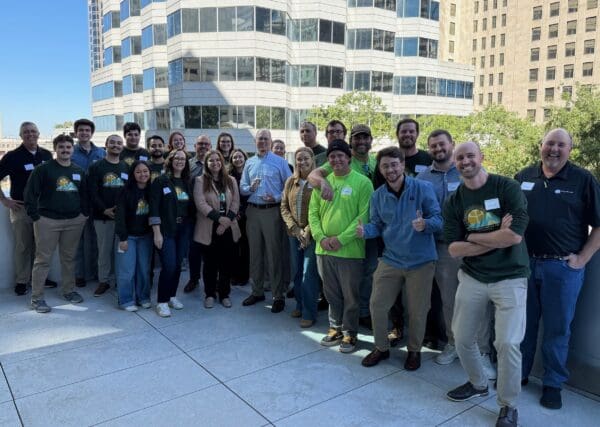A large group of smiling people post on a rooftop patio