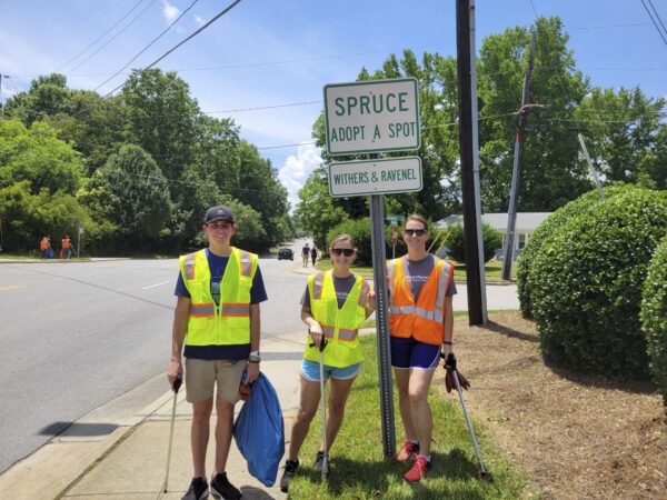 Three people in high-visibility vests next to an Adopt-A-Spot sign