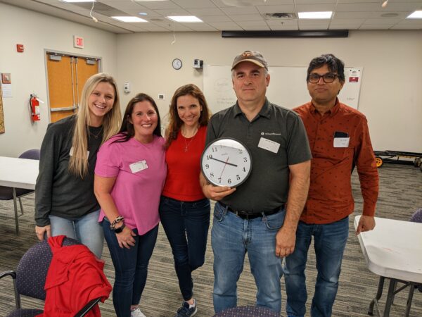 The winning team of a scavenger hunt holding a clock showing their completion time