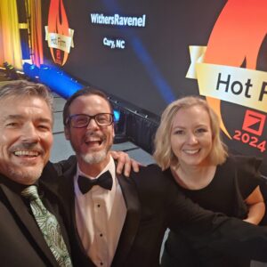 Two formally dressed professionals on stage taking a selfie at an awards banquet.