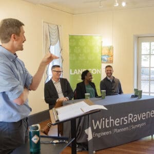 A person speaking at the front of a room to an audience at a lectern.