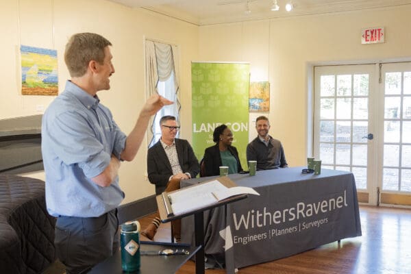 A person speaking at the front of a room to an audience at a lectern.