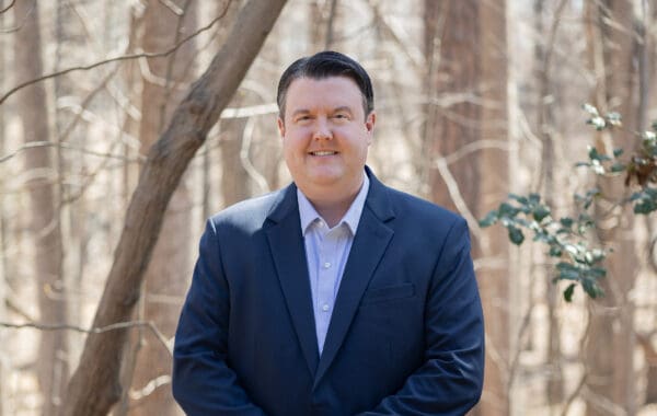David Gale is wearing a dark blue suit and smiling in front of stand of wintry trees