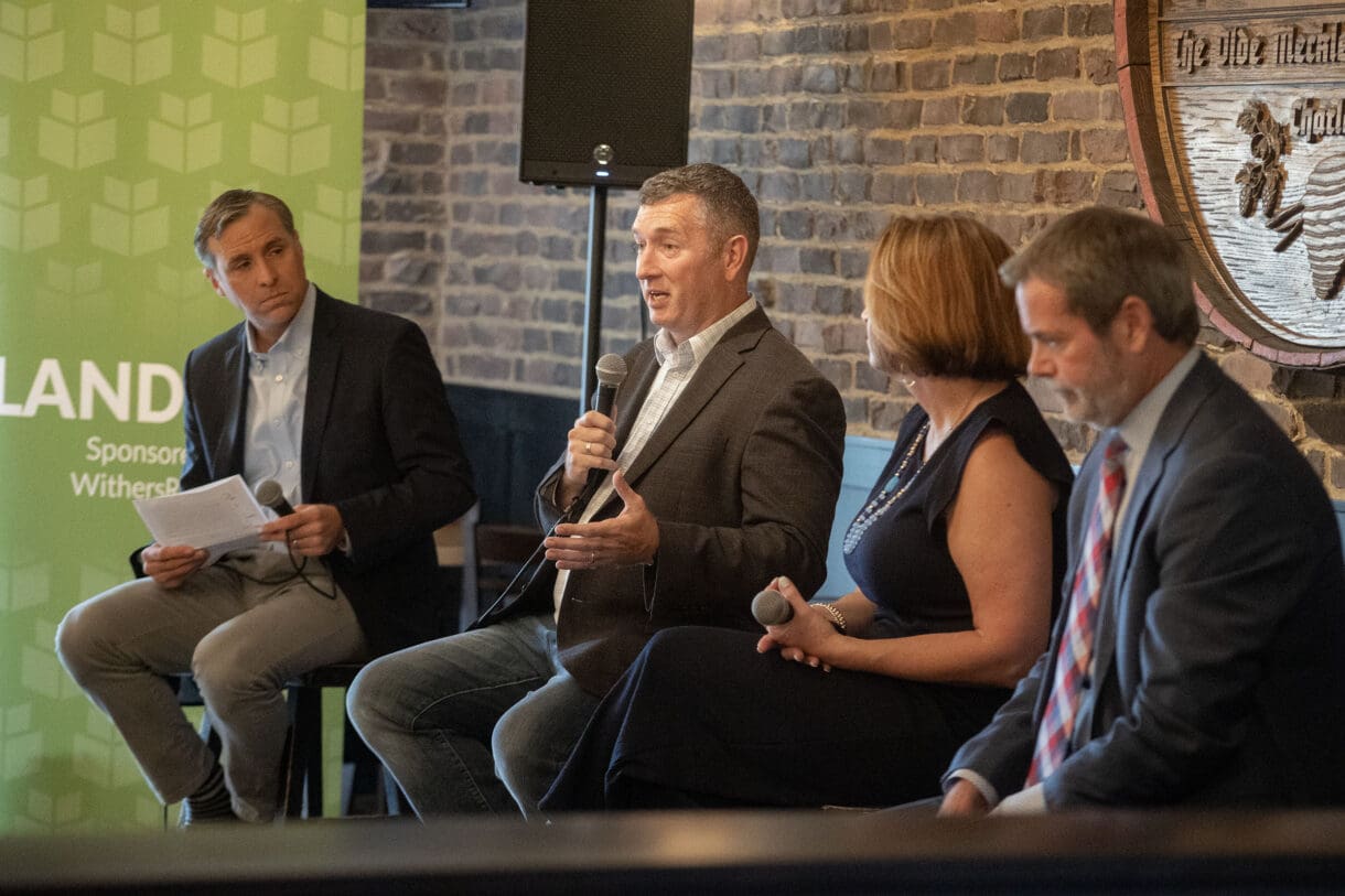 A person holding a microphone while sitting on stage at a panel-led discussion.