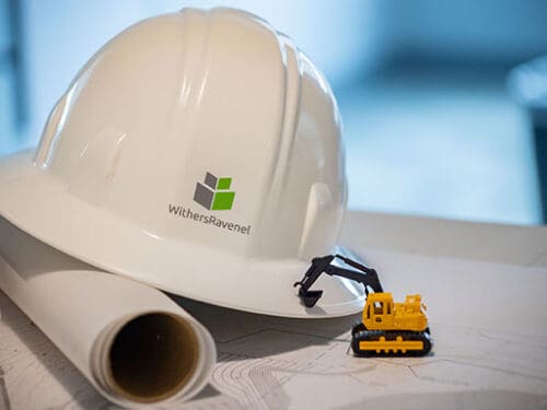 A photo of a hard hat on a table with a set of plans and a toy bulldozer