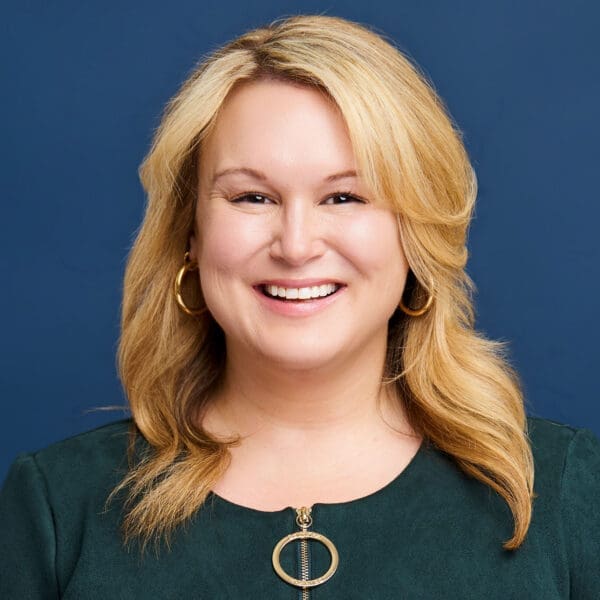 A woman with wavy shoulder-length hair smiles directly at the camera