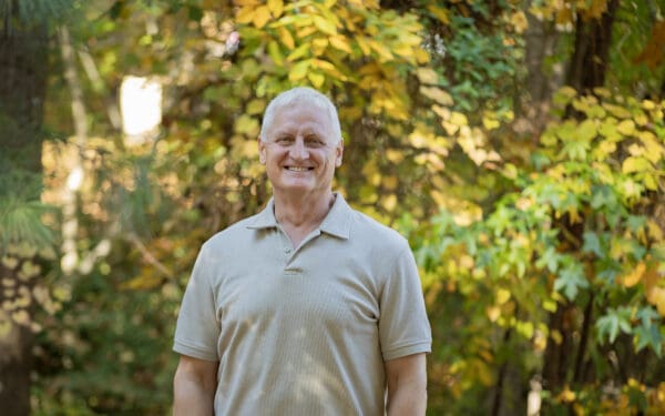 A clean-shaven smiling man in a tan shirt