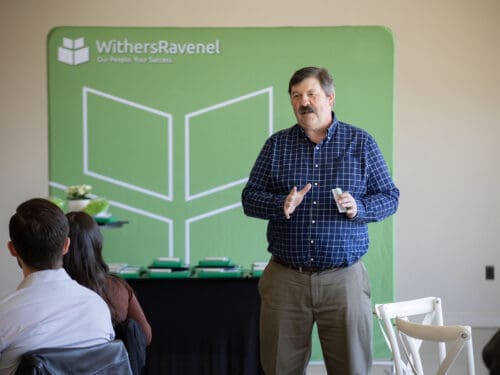 A man speaking at the front of a conference room.