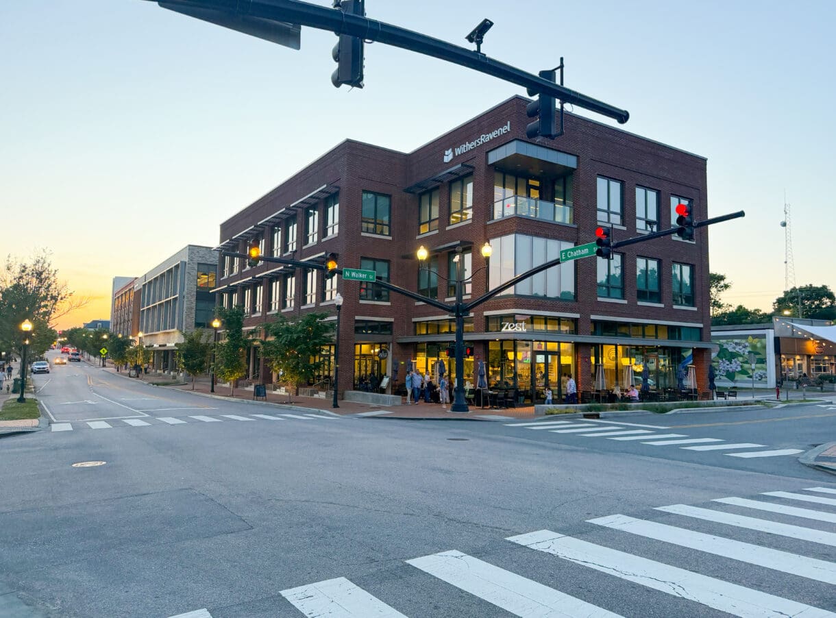 The Rogers Building in downtown Cary, NC, featuring a three-story brick exterior, ground-floor restaurant, and pedestrian-friendly streetscape at a downtown intersection.